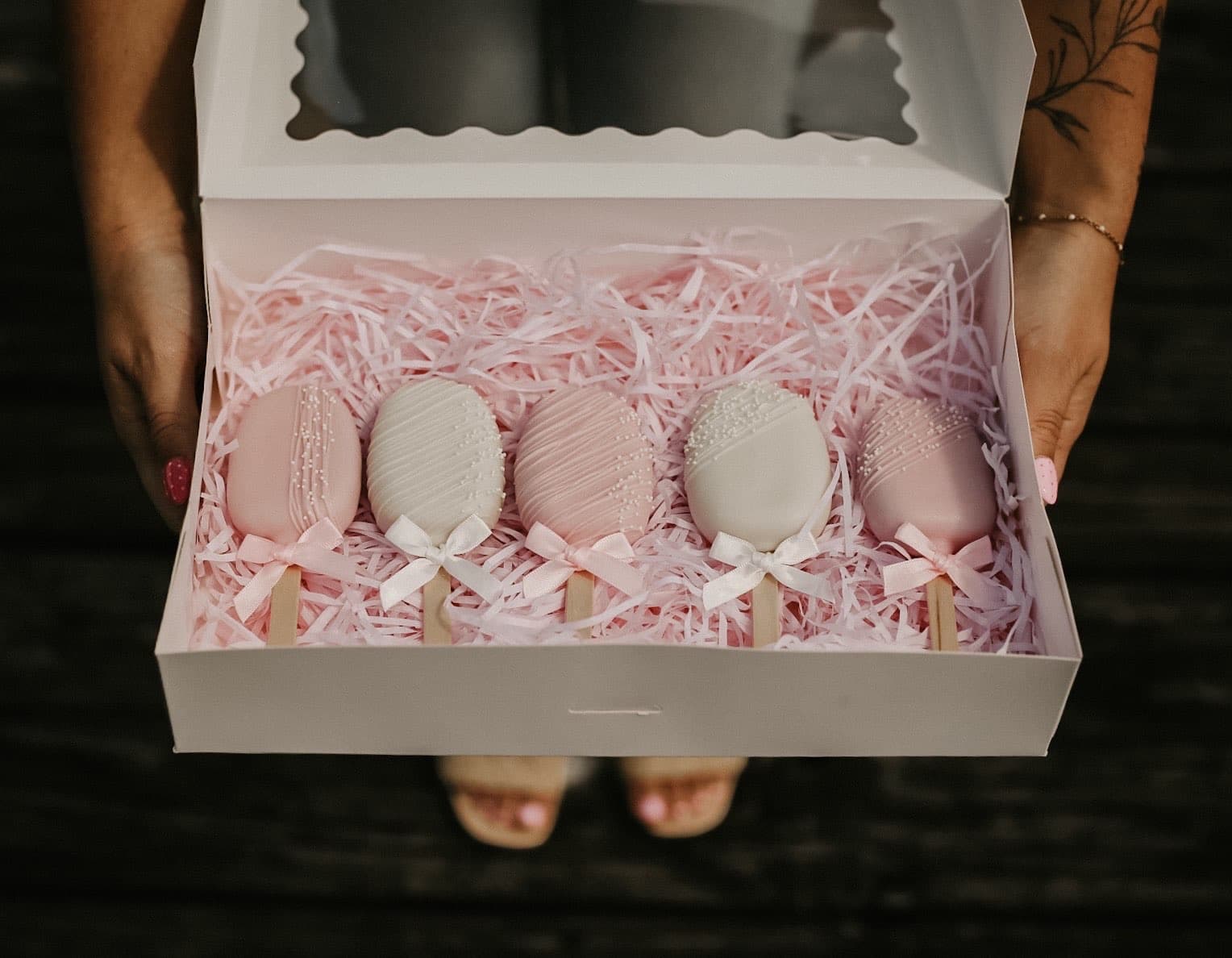A box of blush and ivory cakesicles with satin bows